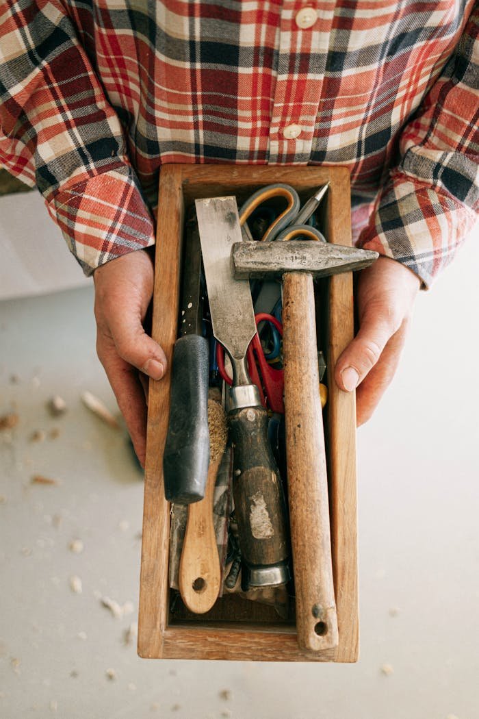 about-img Close-up of tools in a wooden box held by an artisan, showcasing craftsmanship and creativity.