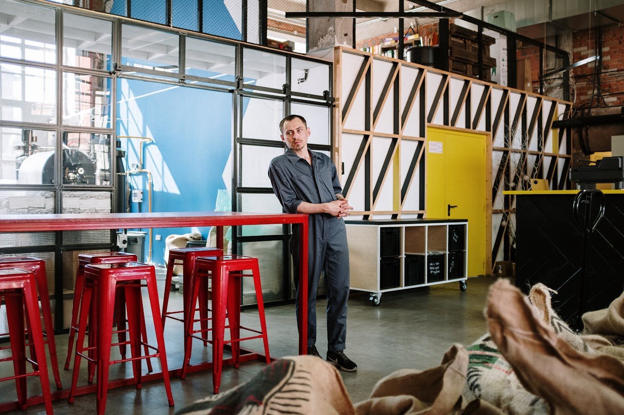 Man in a work uniform in an industrial loft setting with red furniture.