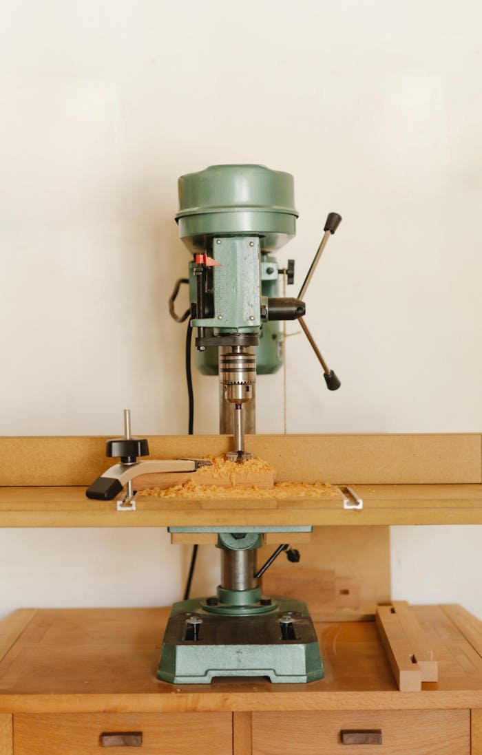 Contemporary drill press for woodwork on timber cabinet near white wall in workroom